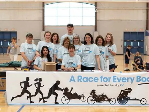 Volunteers standing together behind a table hung with a Unified 5K A Race for Every Body banner