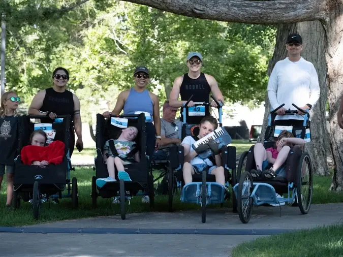 A row of duo teams waiting in the shade of a tree, each rider seated in a running chair